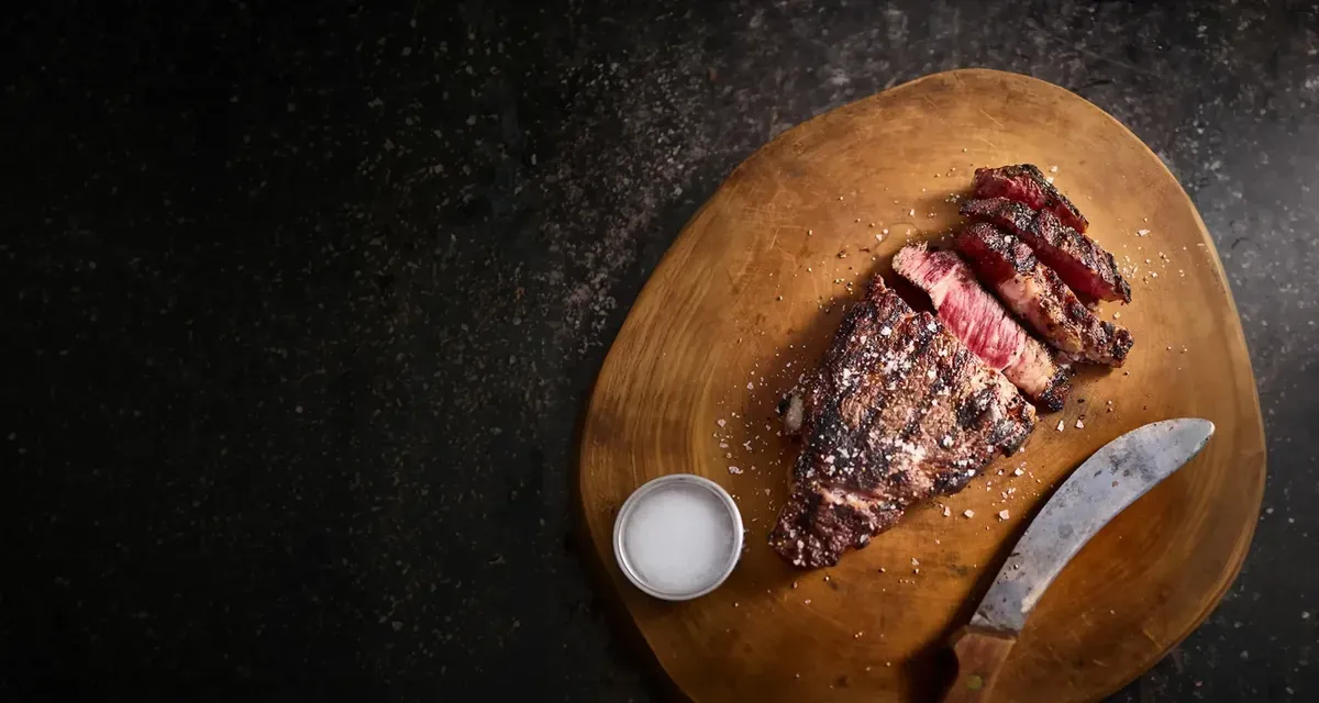 A sliced, seasoned steak on a wooden board with a carving knife